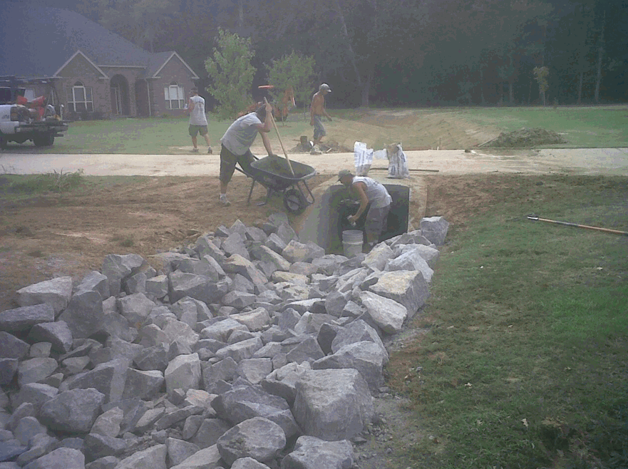 A group of people are working on a rock wall in front of a house.