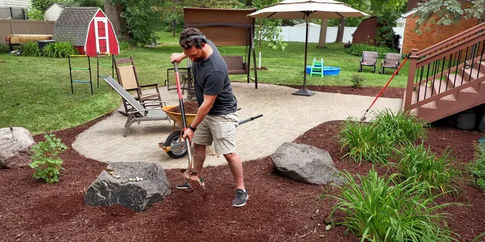A man is using a shovel in a backyard.