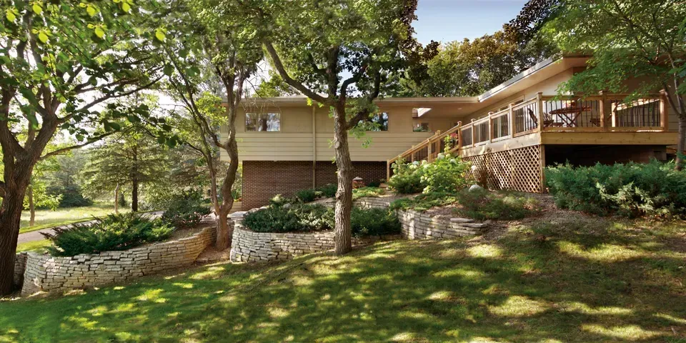 A large house with a large deck is surrounded by trees and grass.