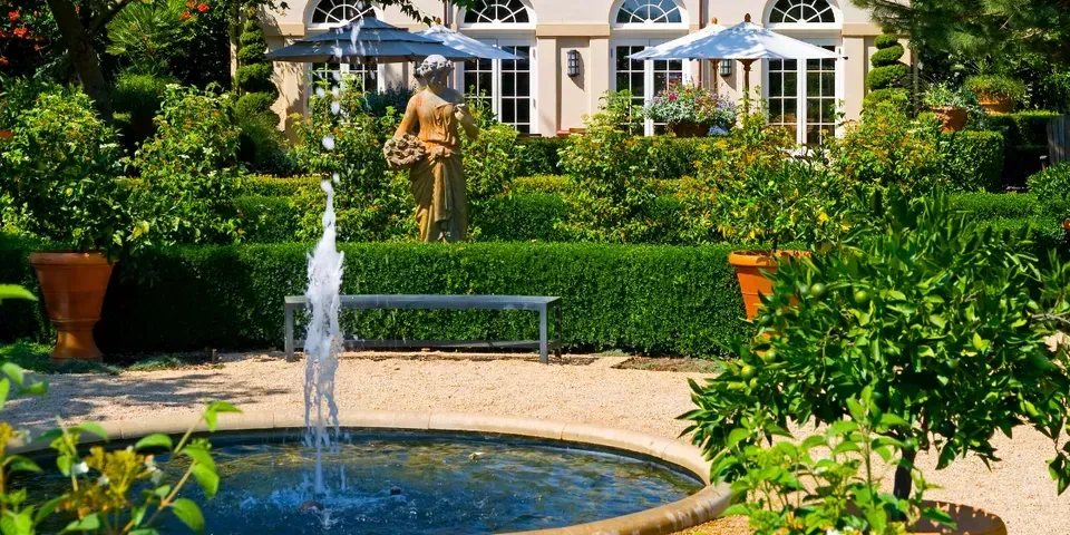A fountain in a garden with a statue in the background.