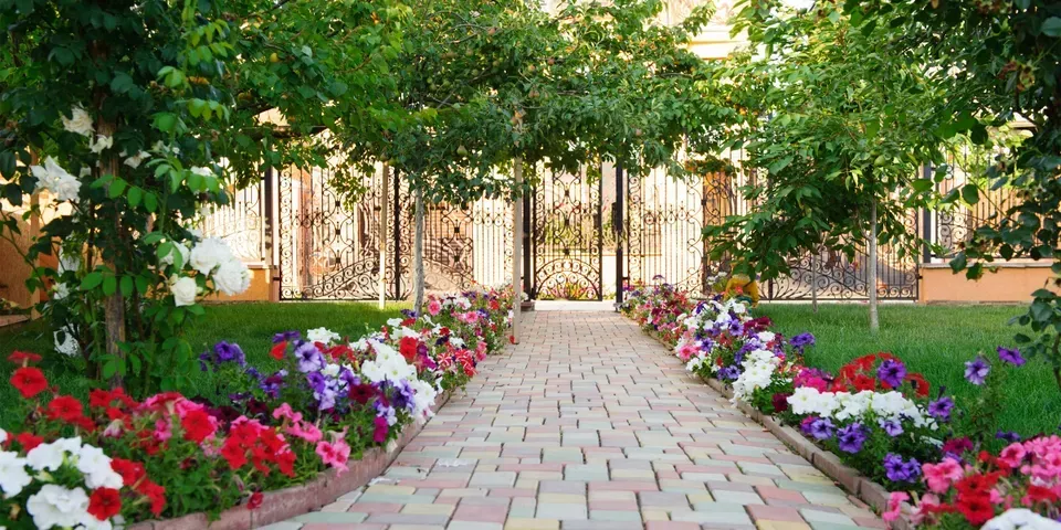 A brick walkway surrounded by flowers and trees in a garden.