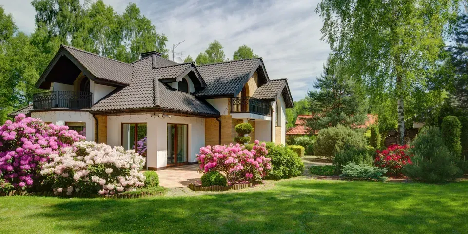 A large house with a lush green lawn and flowers in front of it.