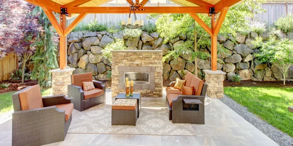 A patio with furniture and a fireplace under a wooden canopy.