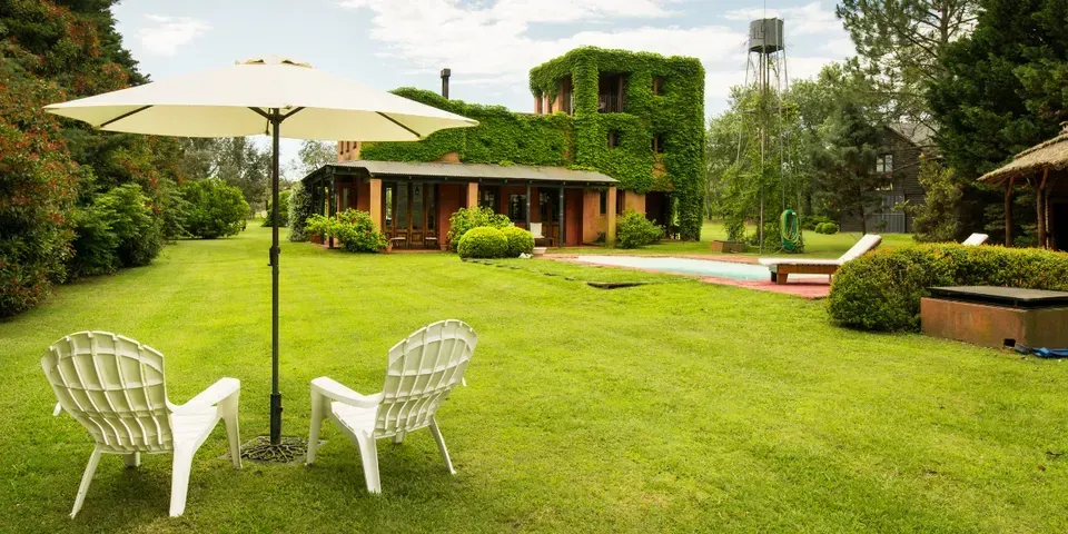 A lawn with chairs and an umbrella in front of a house.
