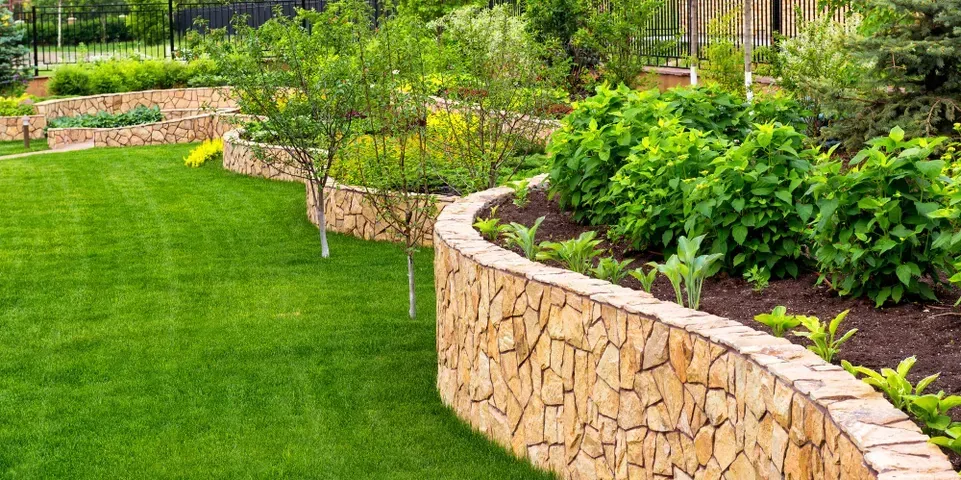 A stone wall surrounds a lush green lawn in a garden.