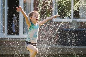 A little girl is playing in a fountain with her arms outstretched.