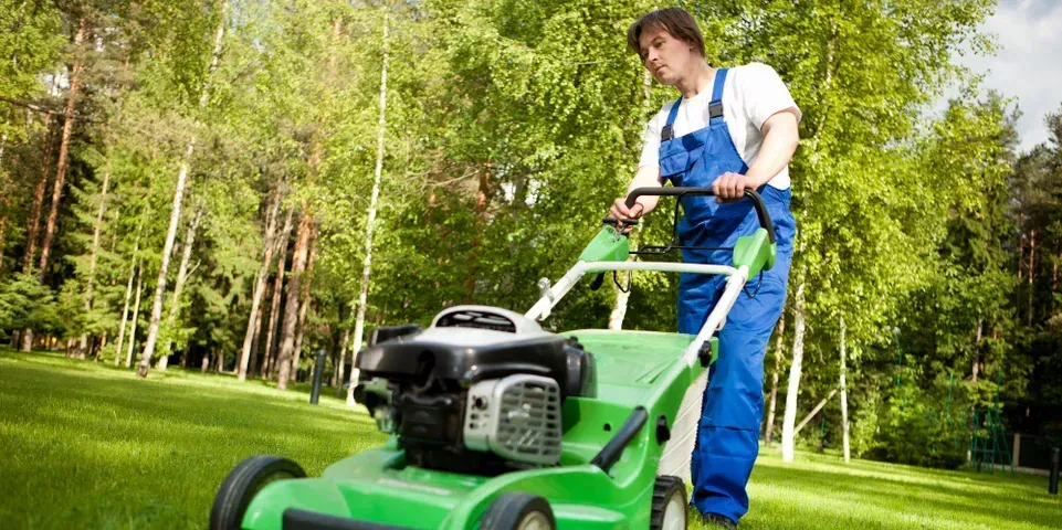 A man is cutting the grass with a green lawn mower.