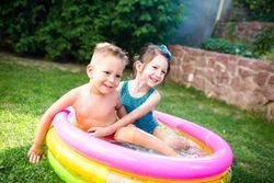 A boy and a girl are playing in an inflatable pool.