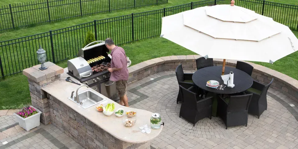 A man is grilling food on a patio with a table and chairs.