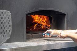 A person is taking a pizza out of a pizza oven.