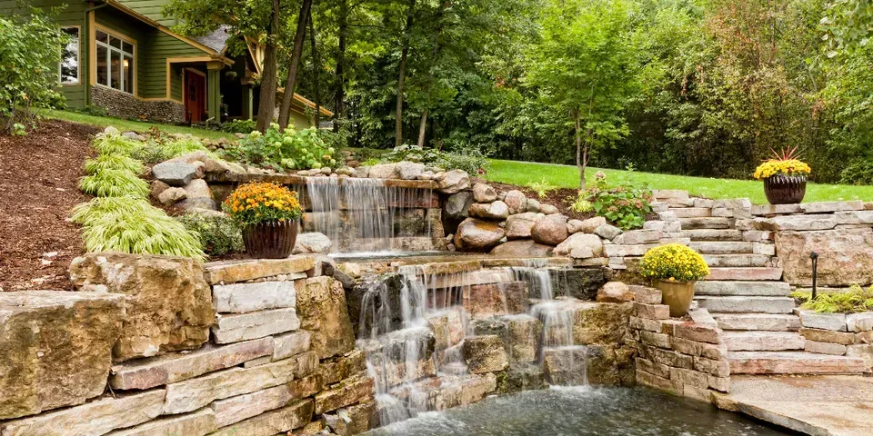 A waterfall is surrounded by rocks and stairs in a backyard.