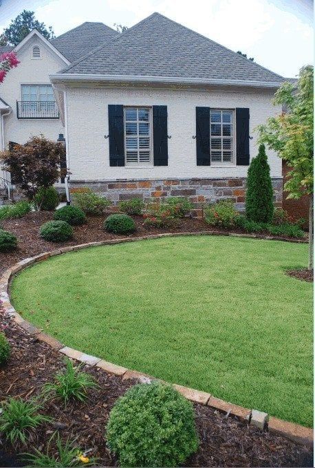 A white house with black shutters and a lush green lawn