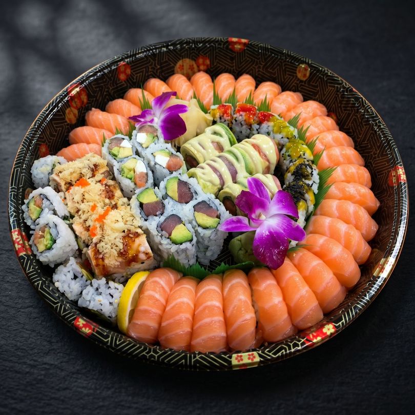 Assorted sushi rolls and salmon sashimi arranged in a decorative bowl with purple orchid flowers