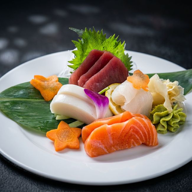 Assorted sushi and sashimi on a white plate with green garnish and star-shaped orange carrot slices