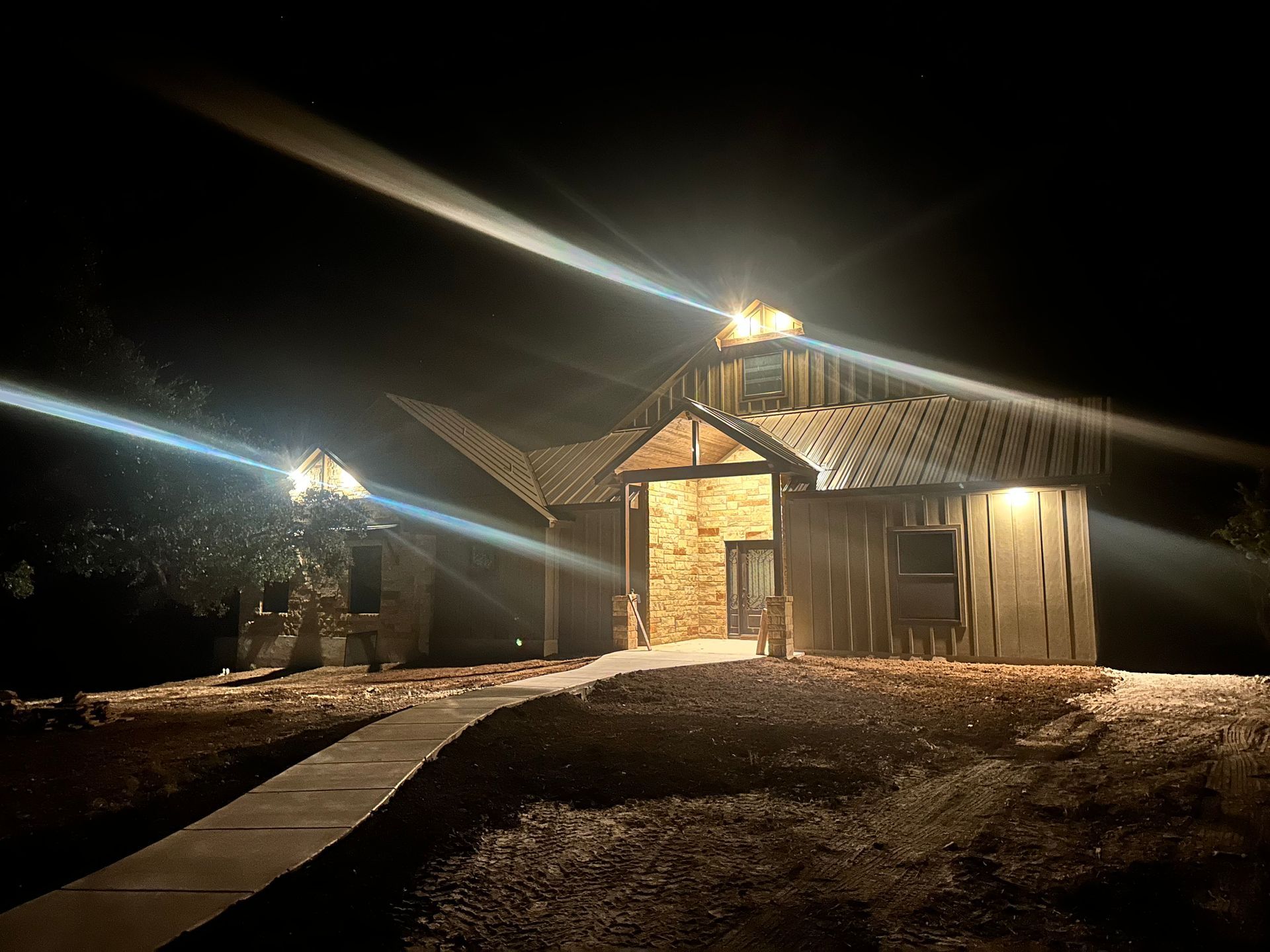 Lit cabin at night with glowing porch lights and a wooden walkway leading to the entrance
