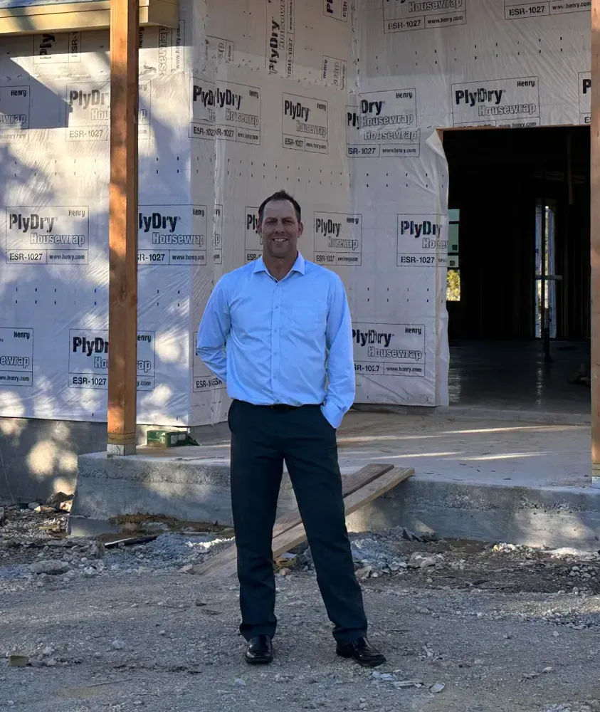 Man standing at a building under construction, wearing a light blue shirt and dark pants.