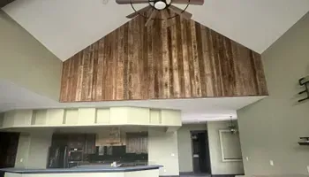 Empty room with vaulted wood ceiling, fan, kitchen counter, and doorway underneath