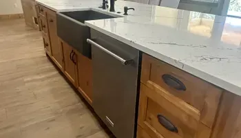 Kitchen island with wood cabinets, white countertop, and built-in dishwasher on hardwood floor