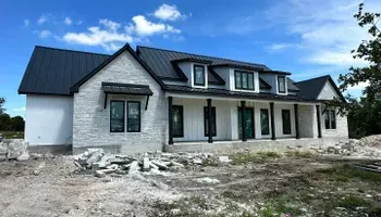 New stone-and-black-roof house under construction on a cleared lot