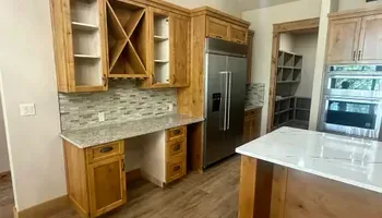 Modern kitchen with wood cabinets, stainless steel fridge, tile backsplash, and white island countertop