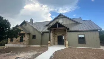 Modern single-story house exterior with gray metal roof, stone accents, and a concrete walkway