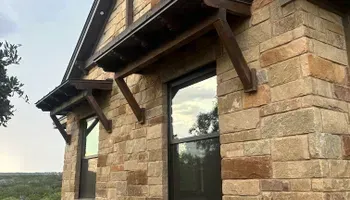 Stone exterior wall with black-framed windows and wooden awning brackets on a house