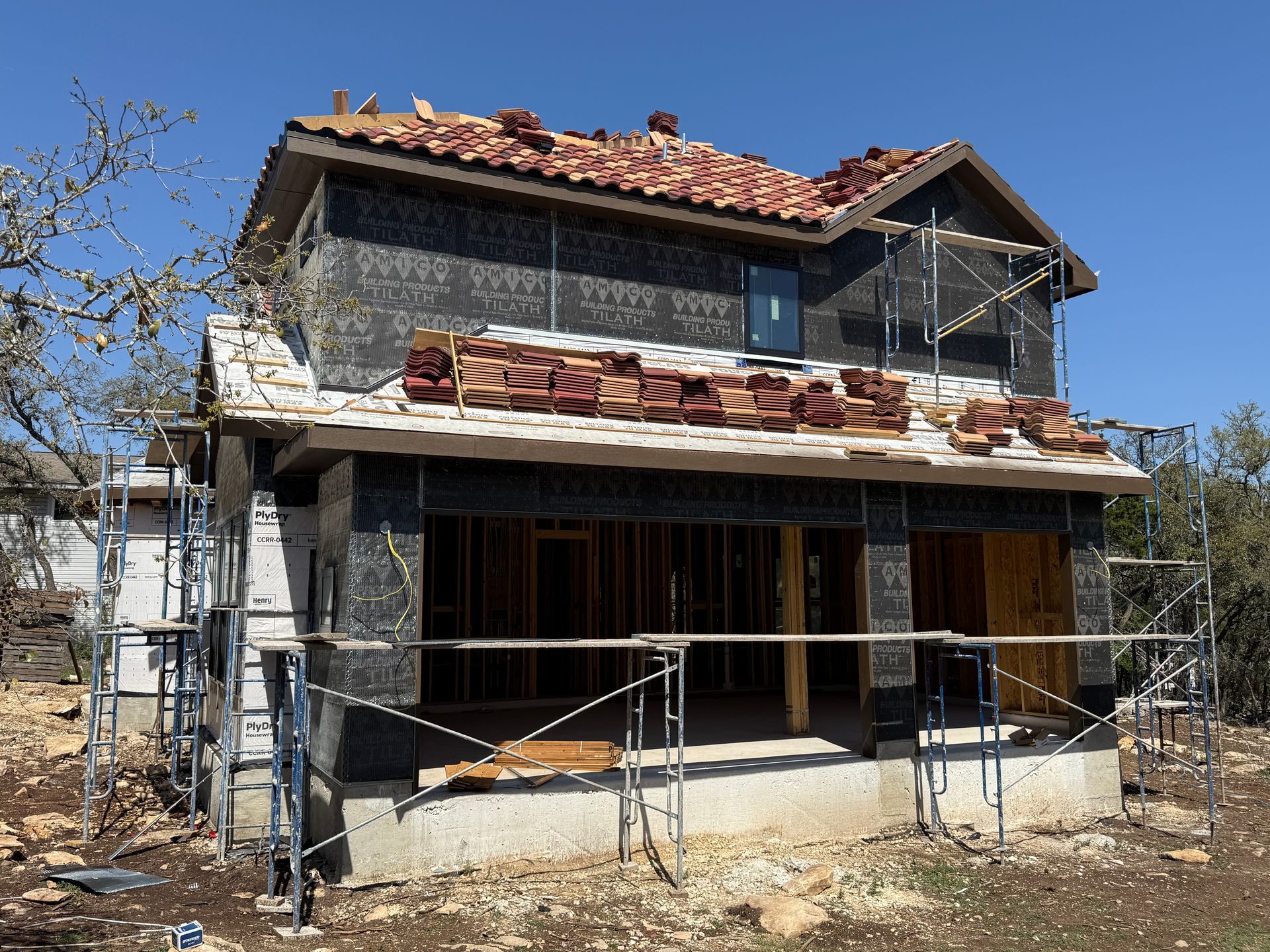 Partially renovated two-story house with scaffolding and exposed roof tiles under a blue sky