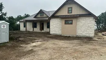 Unfinished stone house with brown trim and dirt yard, viewed from the front under cloudy skies