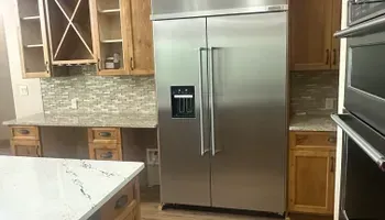 Modern kitchen with stainless steel French door refrigerator, wood cabinets, and marble island countertop