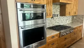 Kitchen with stainless steel double oven, gas range, and wooden cabinets with tiled backsplash.