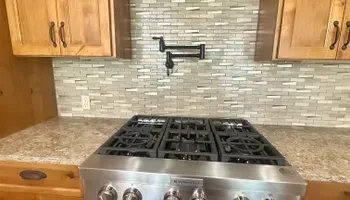 Kitchen backsplash with granite countertop and stainless steel gas stove beneath wooden cabinets.