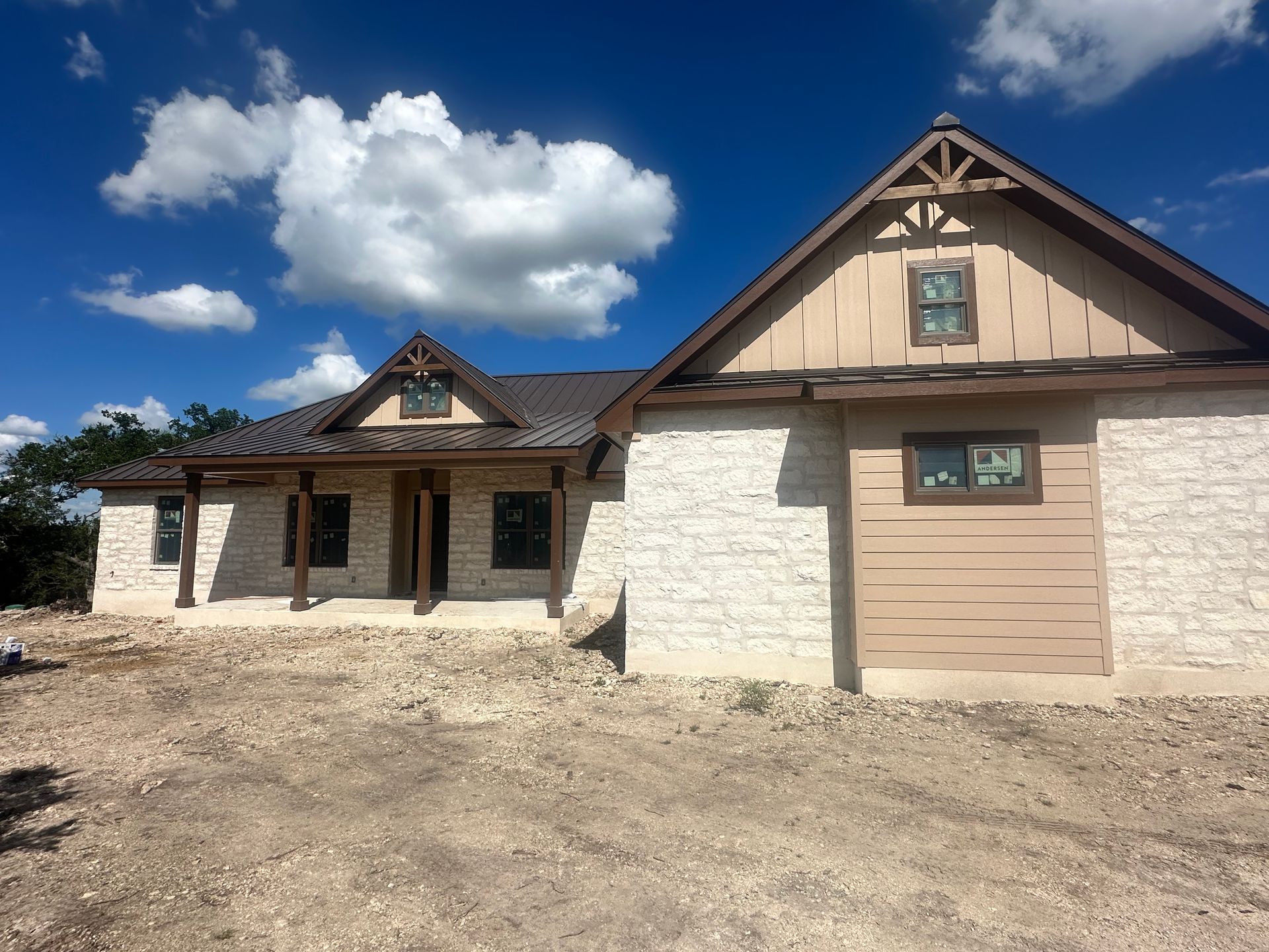 Two-story rustic stone house with tan garage and blue sky with clouds