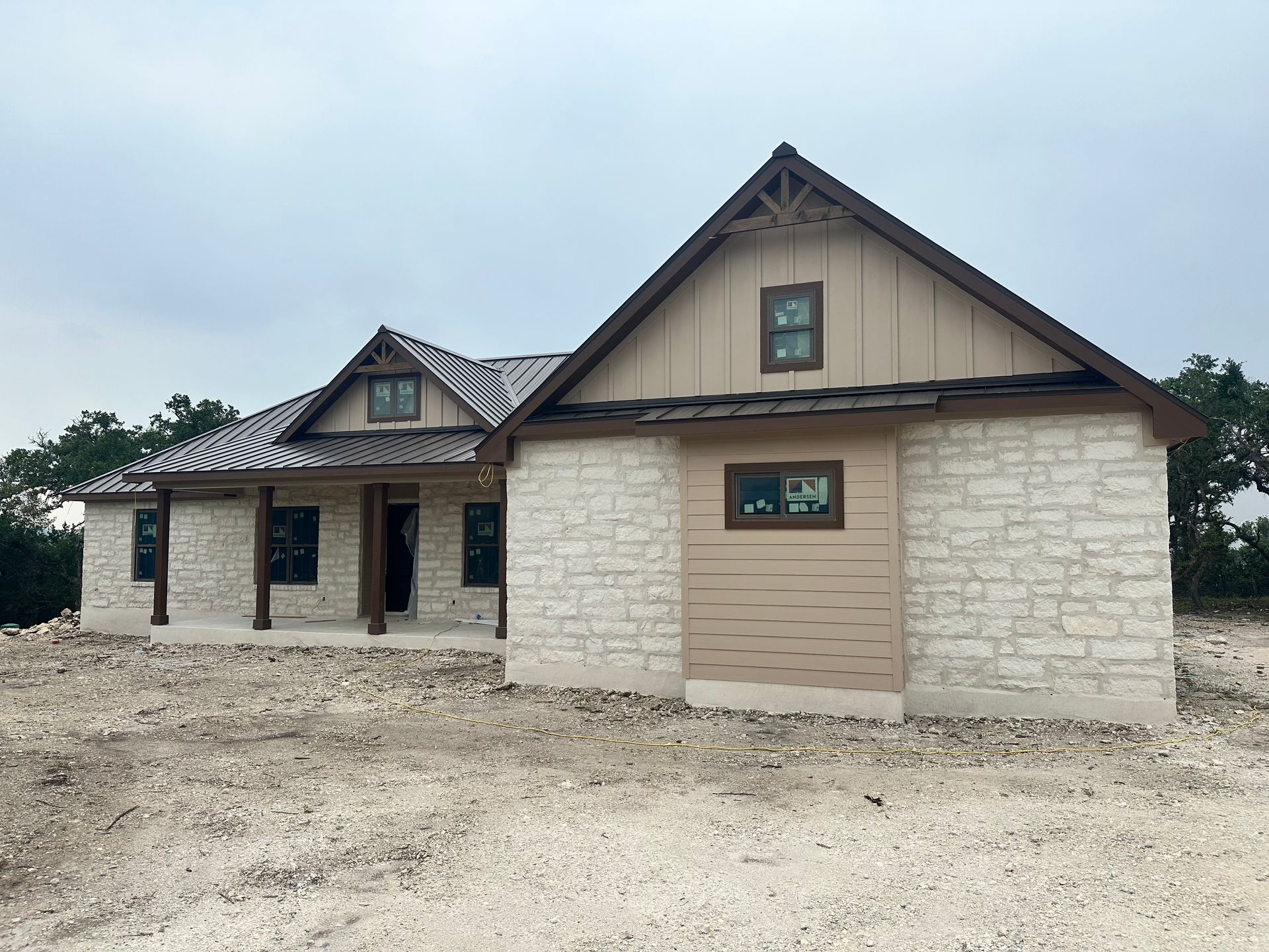 Stone-and-beige house exterior with gabled roof and unfinished dirt foreground.