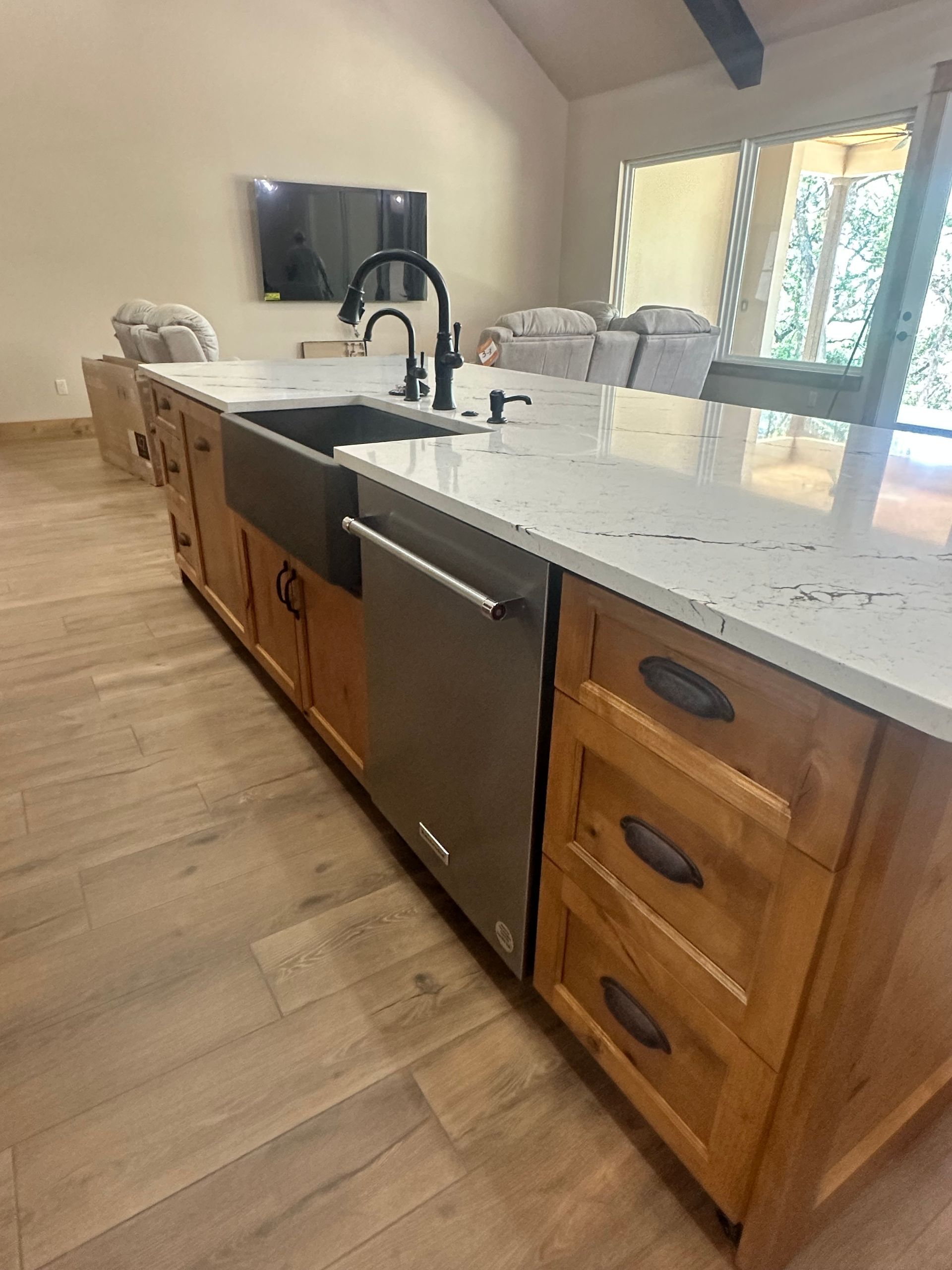 Modern kitchen island with white countertop, black sink, wooden cabinets, and stainless dishwasher beside a window.