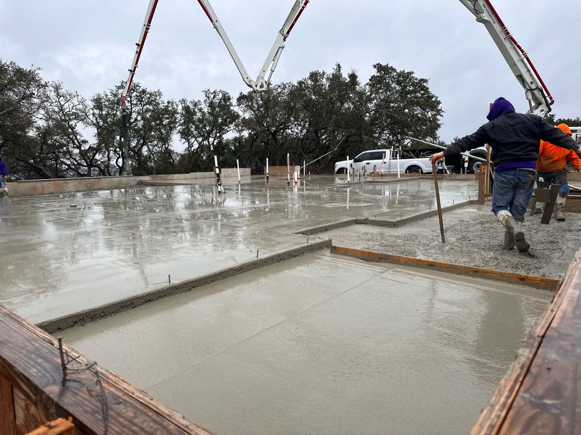 Workers pouring concrete into a foundation slab on a rainy construction site
