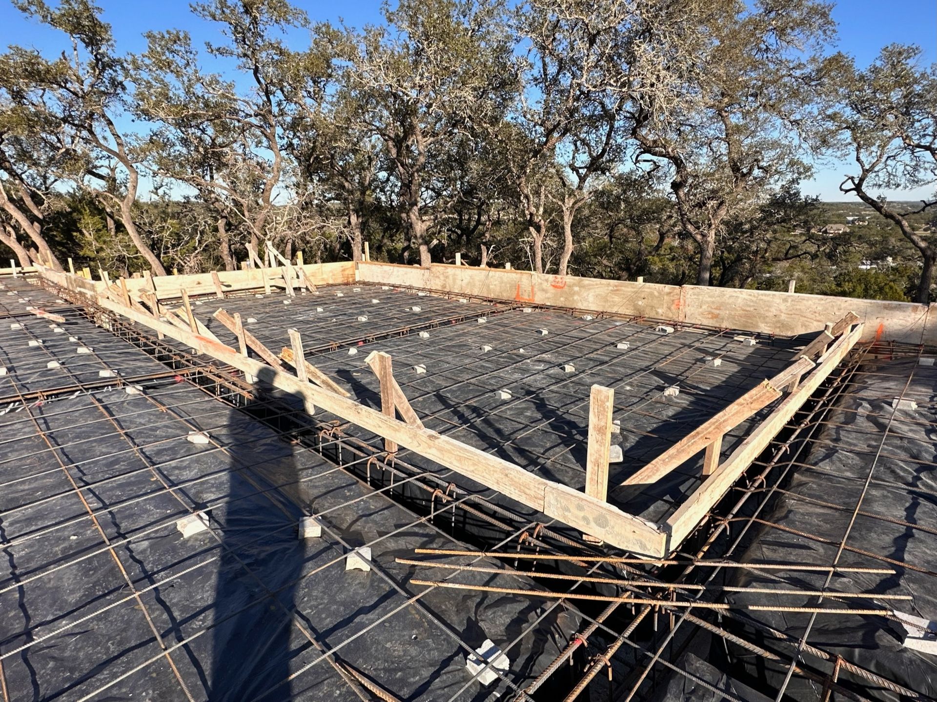 Roof under construction with black underlayment, wooden framing, and trees in the background