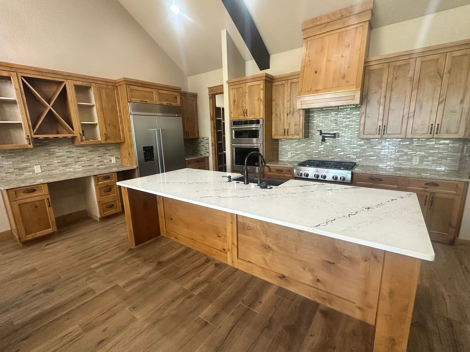 Modern kitchen with wood cabinets, white island countertop, stainless appliances, and tiled backsplash