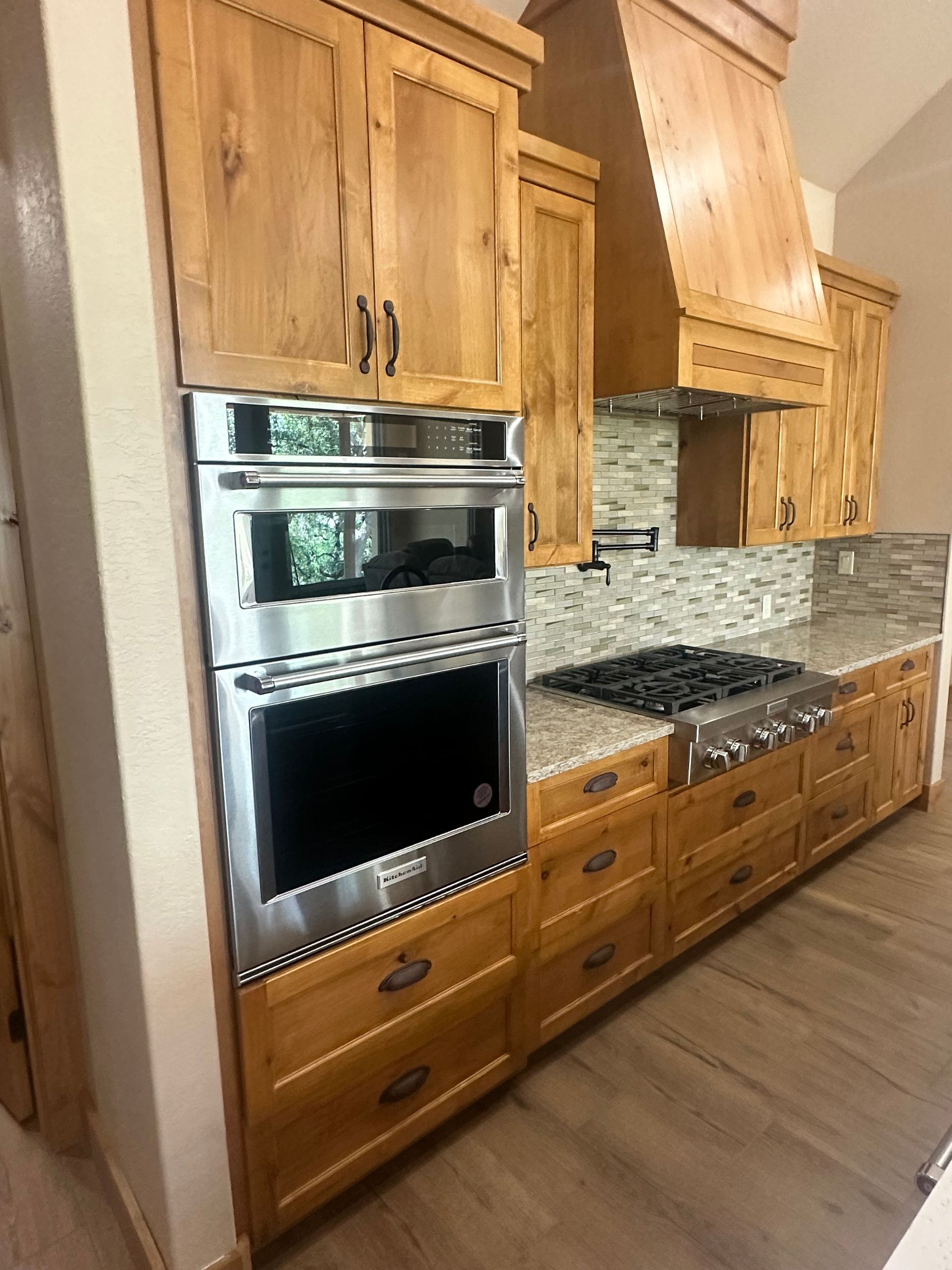 Wooden kitchen with built-in stainless steel oven, gas cooktop, and mosaic tile backsplash