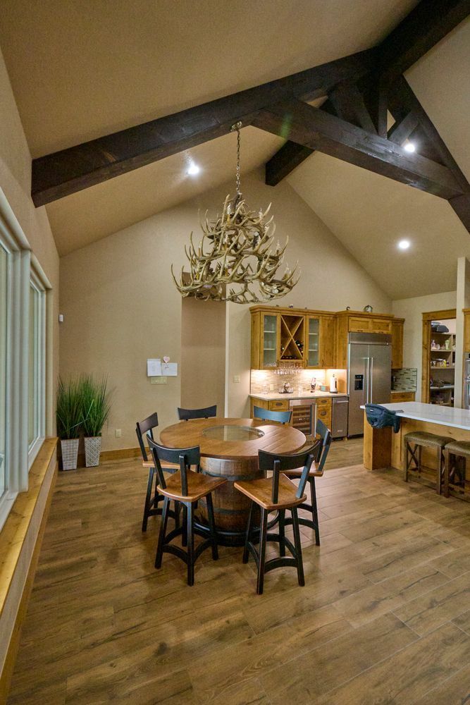 Open dining room with wooden table, chairs, chandelier, and exposed beams under a vaulted ceiling.