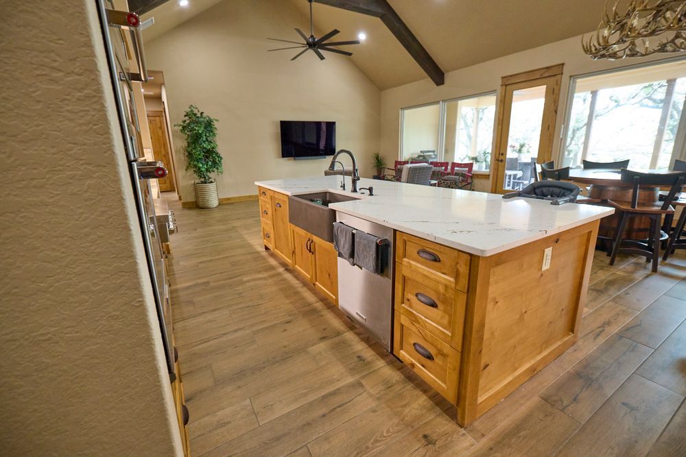 Open kitchen with a large island, wood cabinets, stainless dishwasher, and vaulted ceiling in a bright home interior