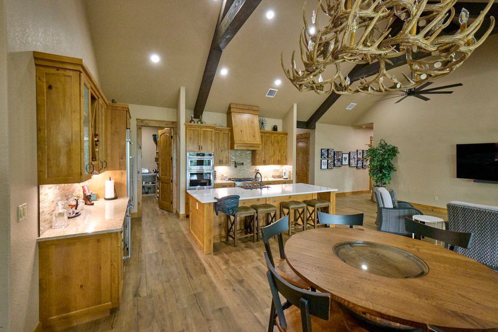 Warm wood kitchen and dining area with island, chandelier, and modern chairs in a cozy open-plan home