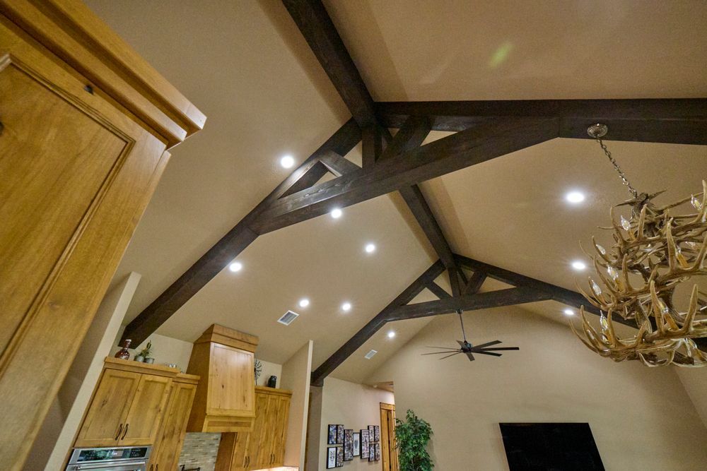 Vaulted living room ceiling with dark wood beams, recessed lights, and a decorative chandelier