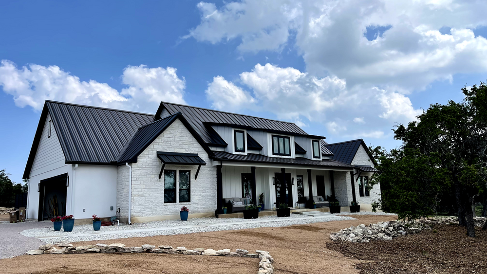 Modern white house with dark roof, large windows, and a front porch under a cloudy sky
