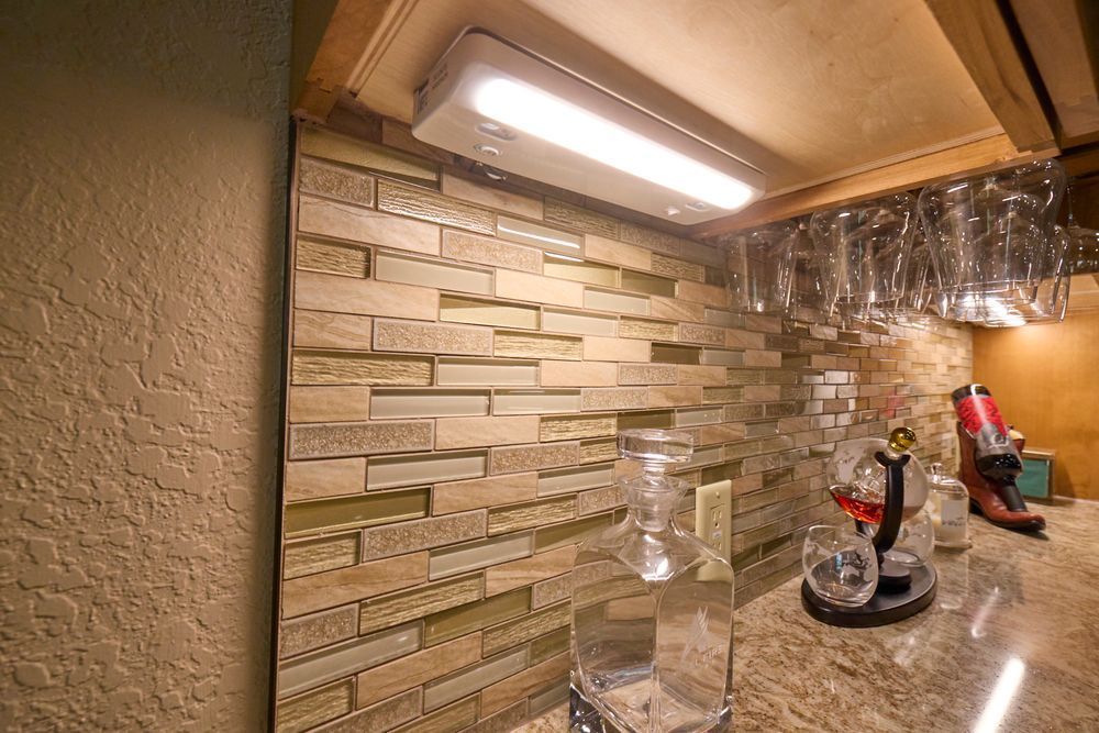 Kitchen backsplash with under-cabinet light, granite counter, and utensils near a tiled wall.