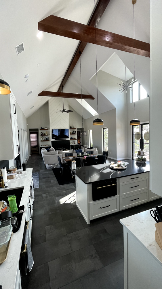Bright modern kitchen with white cabinets, dark floor tiles, island, and exposed wooden beams