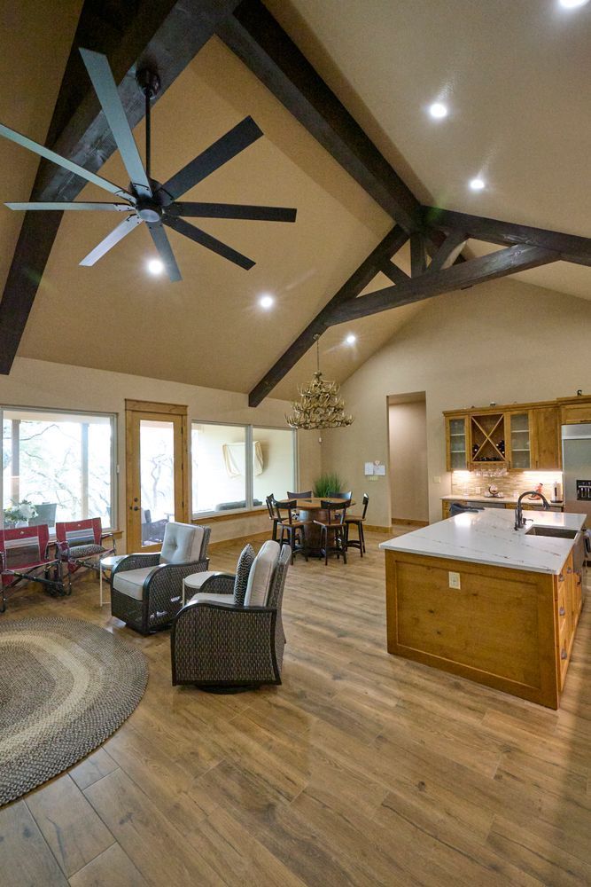 Open-concept living room and kitchen with vaulted wood ceiling, ceiling fans, and large windows