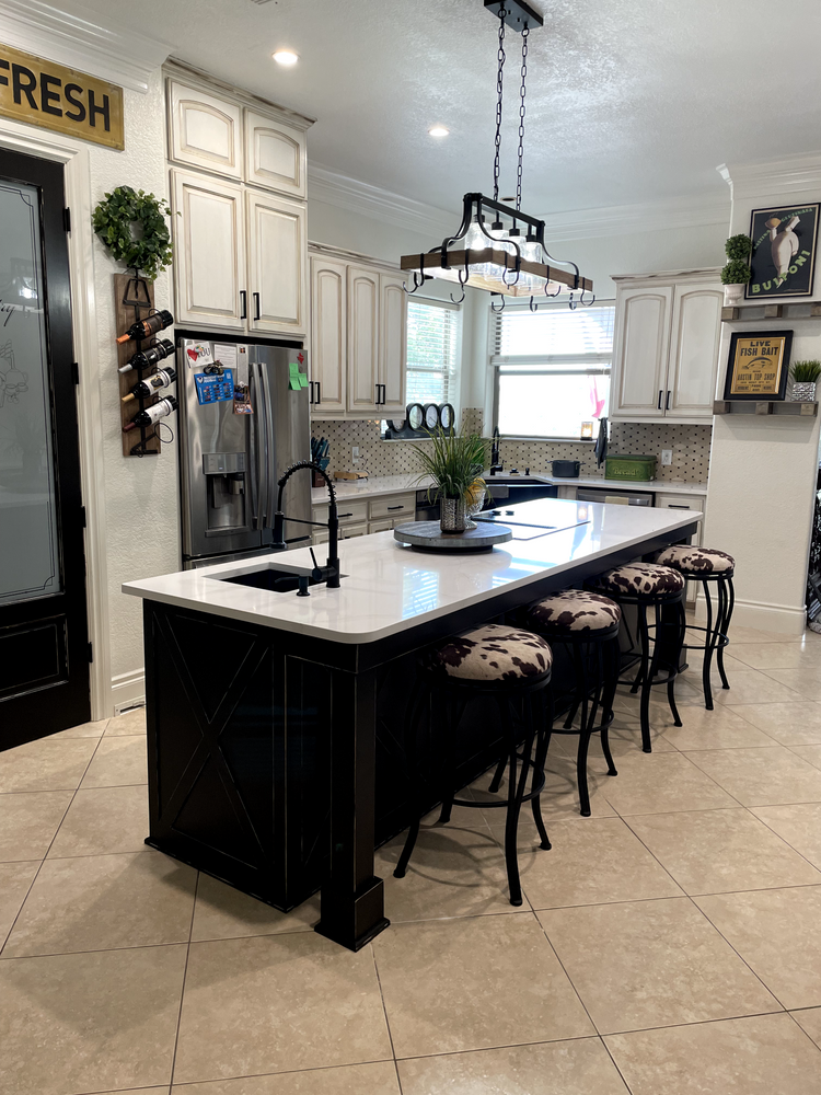 Modern kitchen with large island, black stools, white cabinets, and stainless steel appliances