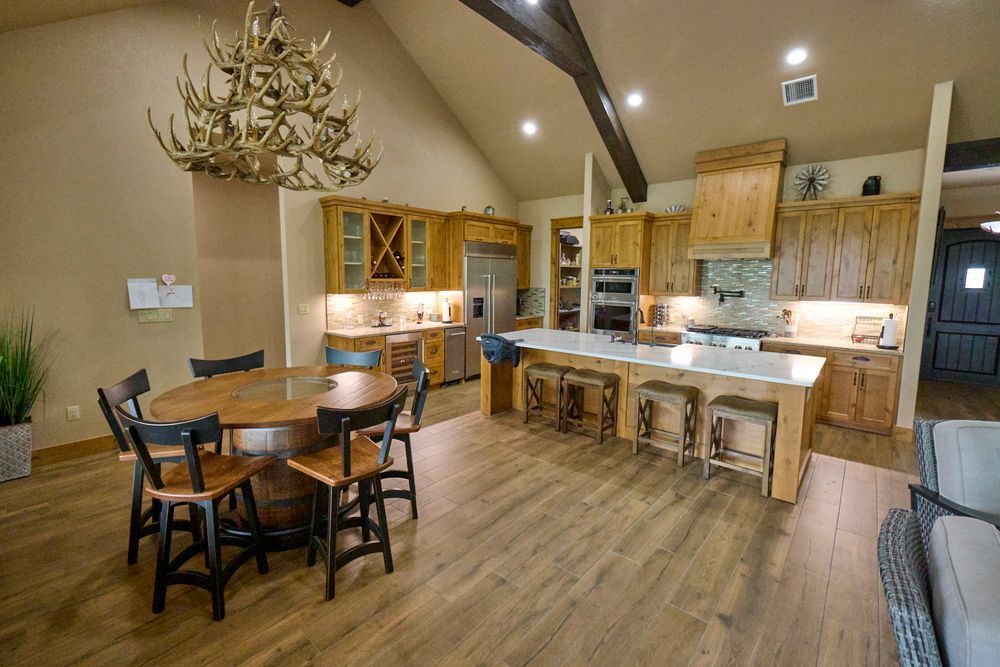 Modern rustic kitchen and dining area with wood cabinets, island stools, and round table with chandelier