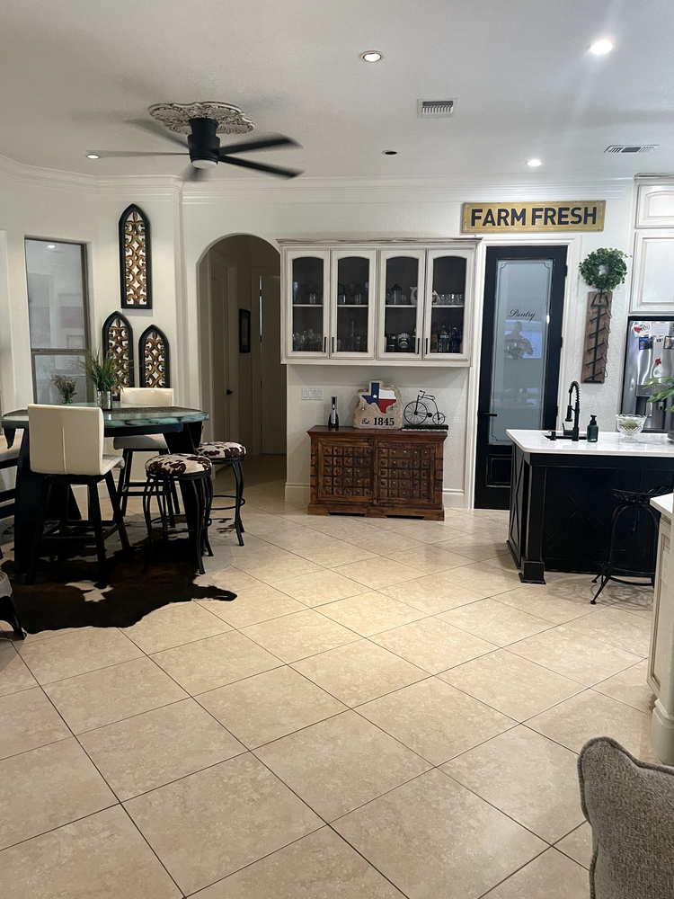 Bright kitchen with white cabinets, tiled floor, black dining set, and a “FARM FRESH” sign on the wall