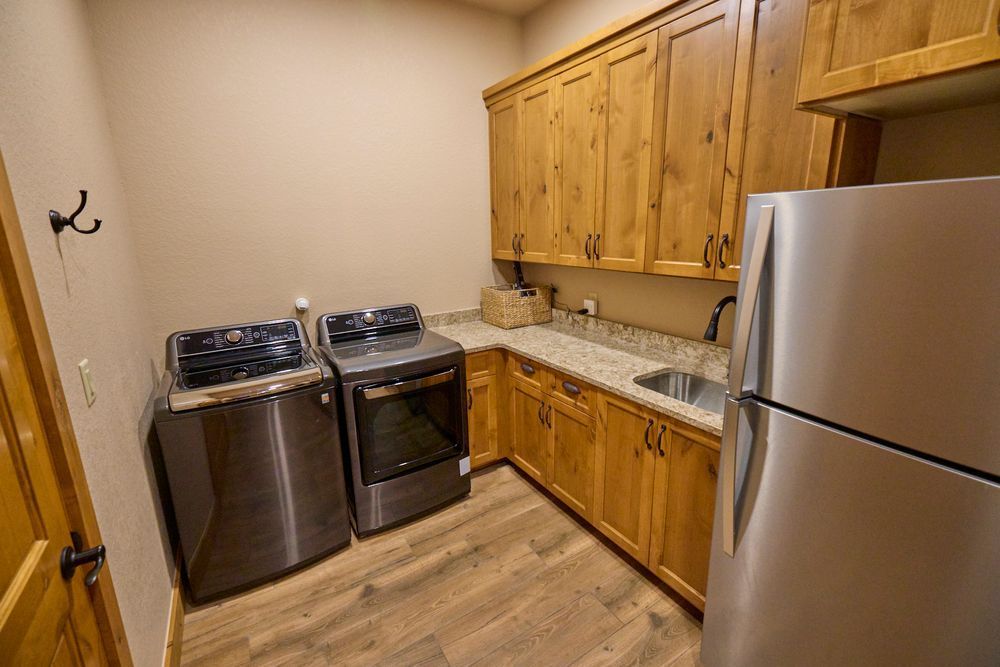 Small kitchen with wood cabinets, stainless fridge, stove, and dark dishwasher on wood-look floor.
